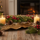 Decorative setting with candles, greenery, and a gold driftwood dish on a wooden surface.