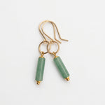 A pair of gold-tone dangle earrings with cylindrical light green stone beads, displayed on a white background