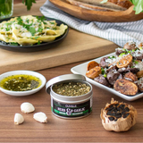 Table with food, herbs, and a container of Olivelle herb and garlic seasoning.