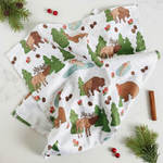 Kitchen towel with forest animal pattern on a white surface with pine branches and berries.