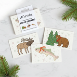 Set of compostable pop-up sponges with animal illustrations on a marble surface with Christmas tree branches.