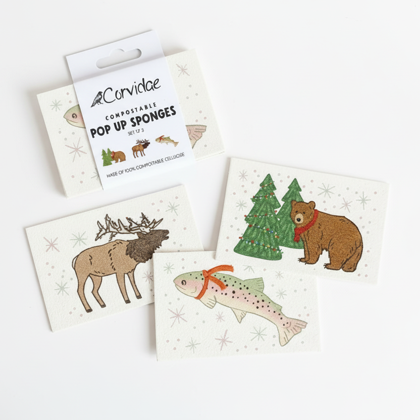 Set of compostable pop-up sponges with animal illustrations on a marble surface with Christmas tree branches.