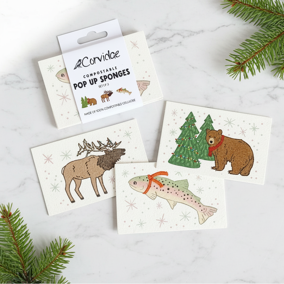 Set of compostable pop-up sponges with animal illustrations on a marble surface with Christmas tree branches.