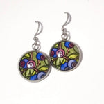 A pair of silver-tone dangle earrings with round glass cabochons featuring a colorful floral and berry pattern in green, blue, purple, and pink, shown on a plain white background.