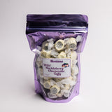 A purple resealable stand-up pouch filled with spiral-shaped Montana Wild Huckleberry Cheesecake Taffy, with a white product label on the front, photographed on a light gray background.