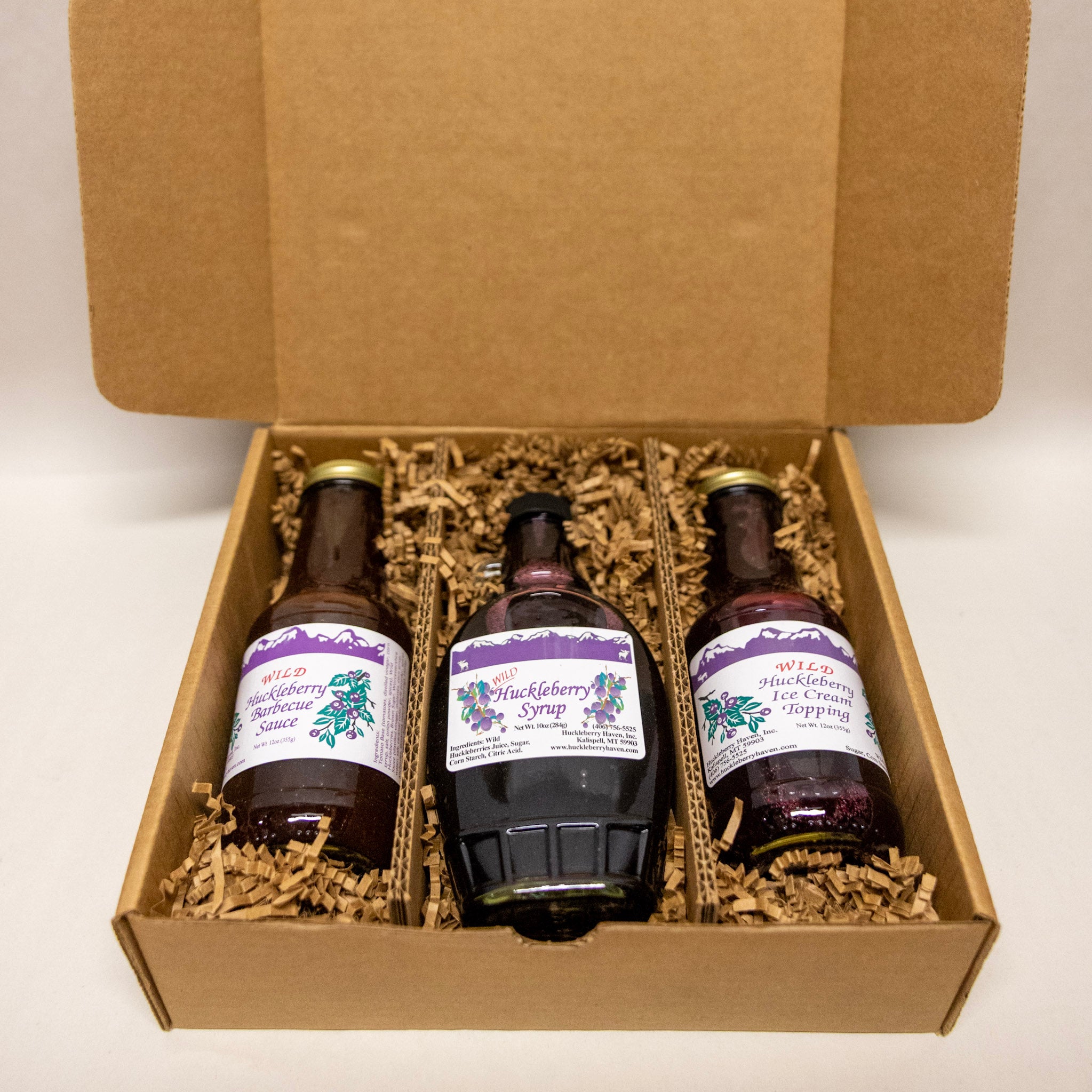 Three bottles of huckleberry gifts in a cardboard box with purple labels.