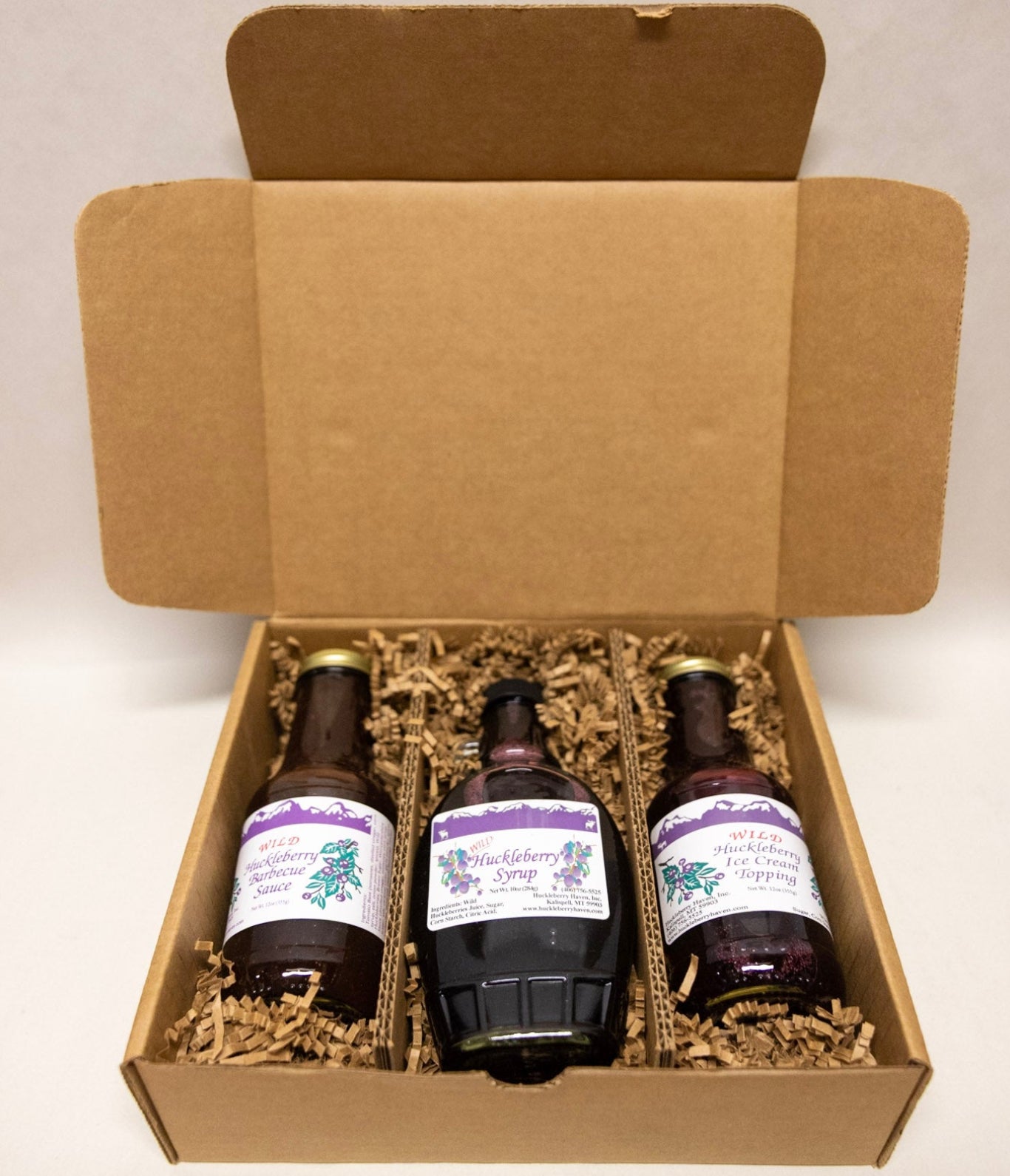 Three bottles of huckleberry product in an open cardboard box with a plain background