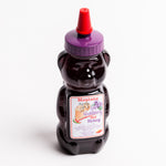 A bear-shaped bottle of Montana Wild Huckleberry Hot Honey, filled with dark purple honey and topped with a purple cap and red nozzle, set against a plain white background.
