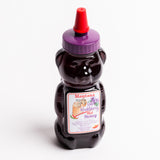 A bear-shaped bottle of Montana Wild Huckleberry Hot Honey, filled with dark purple honey and topped with a purple cap and red nozzle, set against a plain white background.