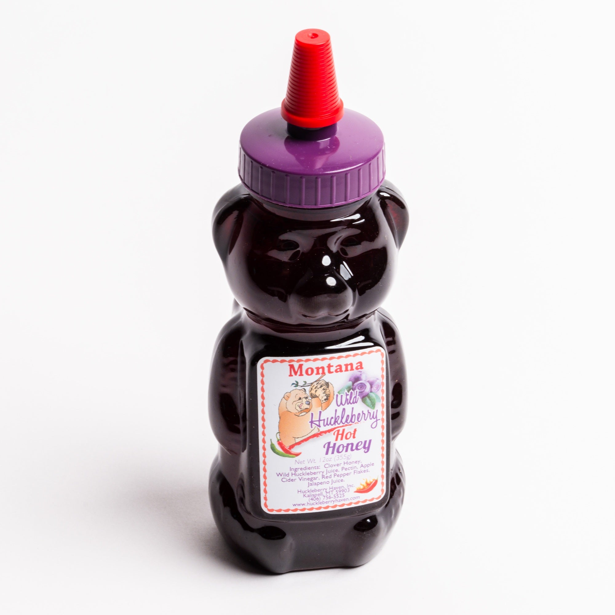 A bear-shaped bottle of Montana Wild Huckleberry Hot Honey, filled with dark purple honey and topped with a purple cap and red nozzle, set against a plain white background.
