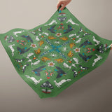 Green fabric with colorful animal and nature pattern held by a hand against a blue background