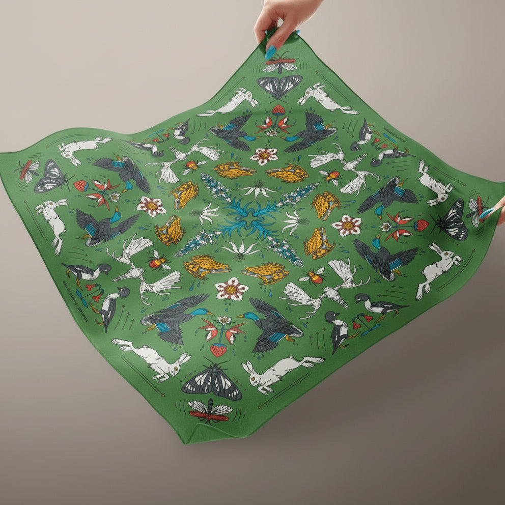 Green fabric with colorful animal and nature pattern held by a hand against a blue background
