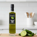 Bottle of Olivelle Jalapeno Lime white balsamic vinegar on a kitchen counter with jalapenos and a lime.
