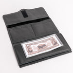 A black leather wallet shown open on a white background, displaying its interior compartments, a black hook-and-loop closure tab, and a clear plastic ID window holding a vintage-style $10 bill.