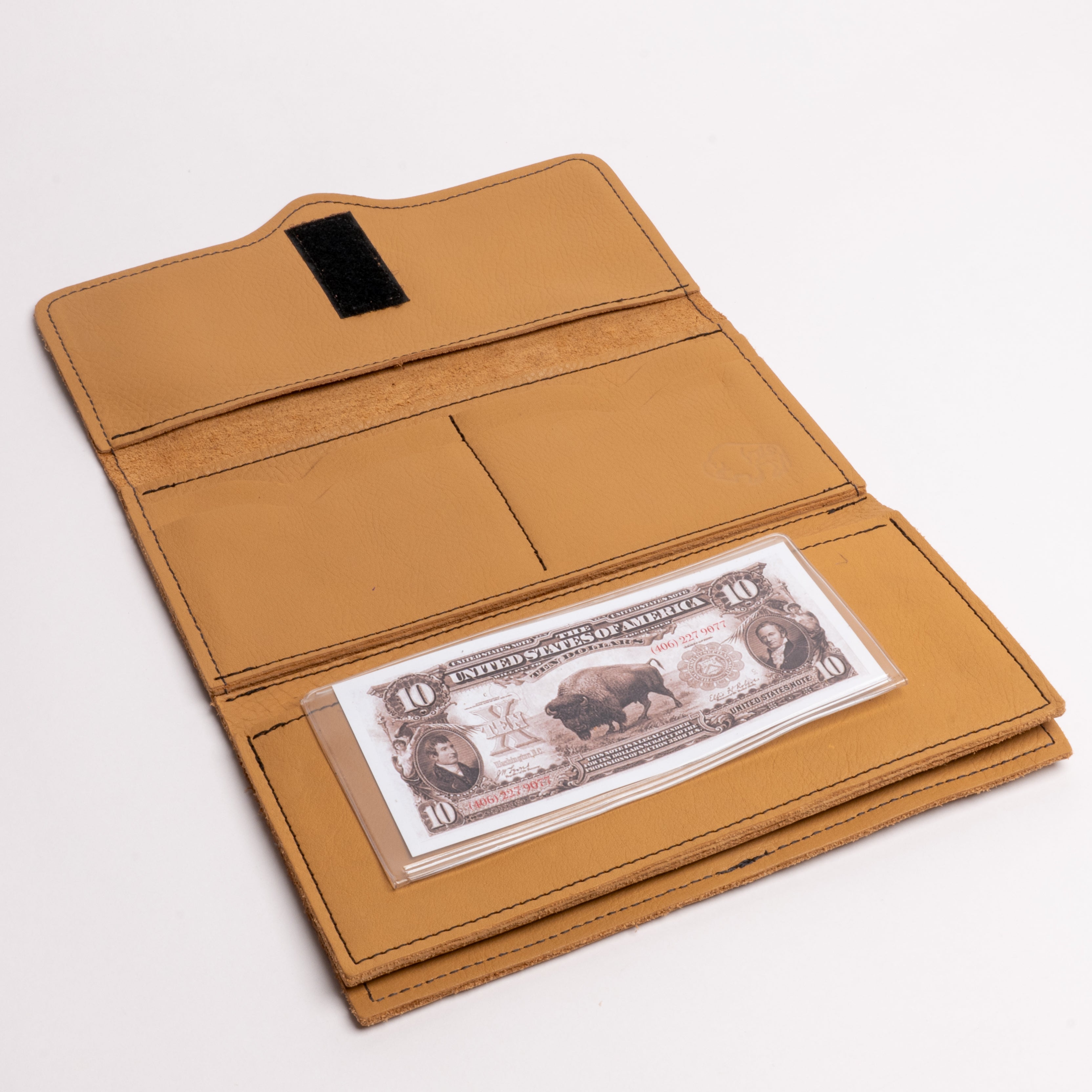 A tan leather wallet shown open on a white background, with a black hook-and-loop closure tab on the inside flap and a stack of U.S.