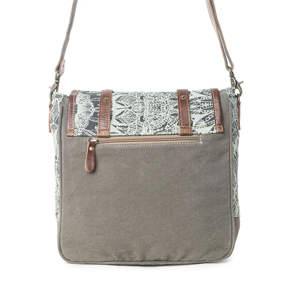 A gray canvas shoulder bag with a patterned flap in black and white, brown leather straps, and a front zippered pocket, shown against a plain white background.