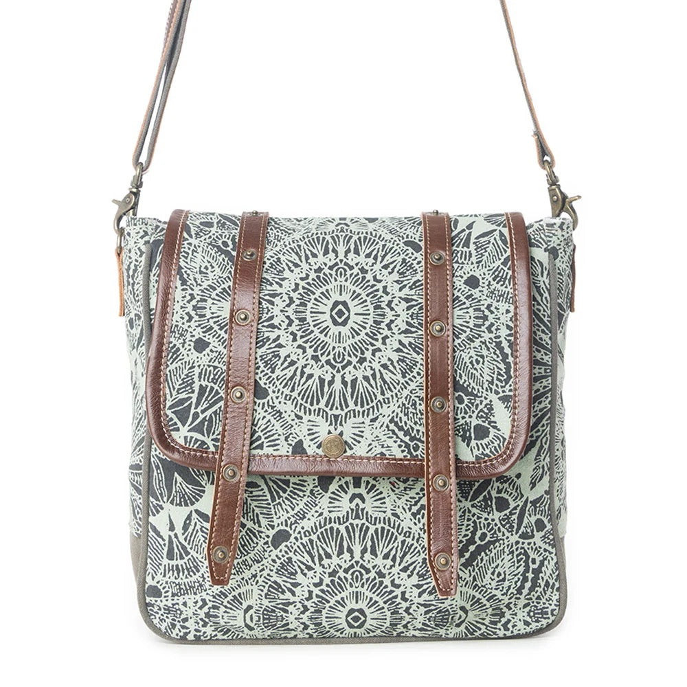A square-shaped shoulder bag with a black and white mandala pattern on a light gray-green background, featuring brown faux-leather straps and metal studs, shown against a plain white background.