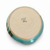 The bottom of a handmade ceramic plate or dish, featuring a light beige clay base with a glossy turquoise blue glaze along the rim and a small dark green patch on the left side. The brand name 'COUNTRY Girl Clay' is printed in black on the center.
