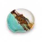 A handmade spoon rest with a unique abstract design, featuring a split design of light turquoise and white on one side, and a textured brown and black organic pattern on the other, shown on a plain white background.