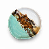 A handmade spoon rest with a unique abstract design, featuring a split design of light turquoise and white on one side, and a textured brown and black organic pattern on the other, shown on a plain white background.