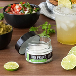 Jar of Lime Fresco salt on a table with guacamole, salsa, and margarita.