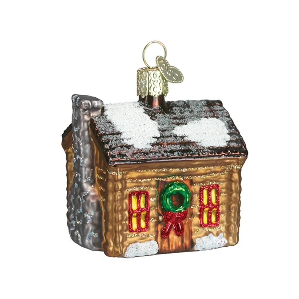 Glass ornament of a cabin with snow on the roof and Christmas decorations on a white background