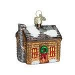 Glass ornament of a cabin with snow on the roof and Christmas decorations on a white background