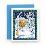A square greeting card with a white border and a colorful winter forest illustration featuring a moose, fox, birch trees, and inspirational text, shown with a blue envelope on a white surface.