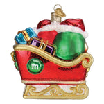 A Christmas ornament shaped like a red sleigh filled with gifts and Santa hats, with a green circle on the side featuring a white lowercase 'm' and a gold hanging loop at the top, shown on a plain white background.