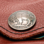 A silver-colored US five-cent coin featuring a buffalo design, resting on a brown textured leather surface.