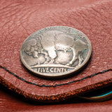 A silver-colored US five-cent coin featuring a buffalo design, resting on a brown textured leather surface.