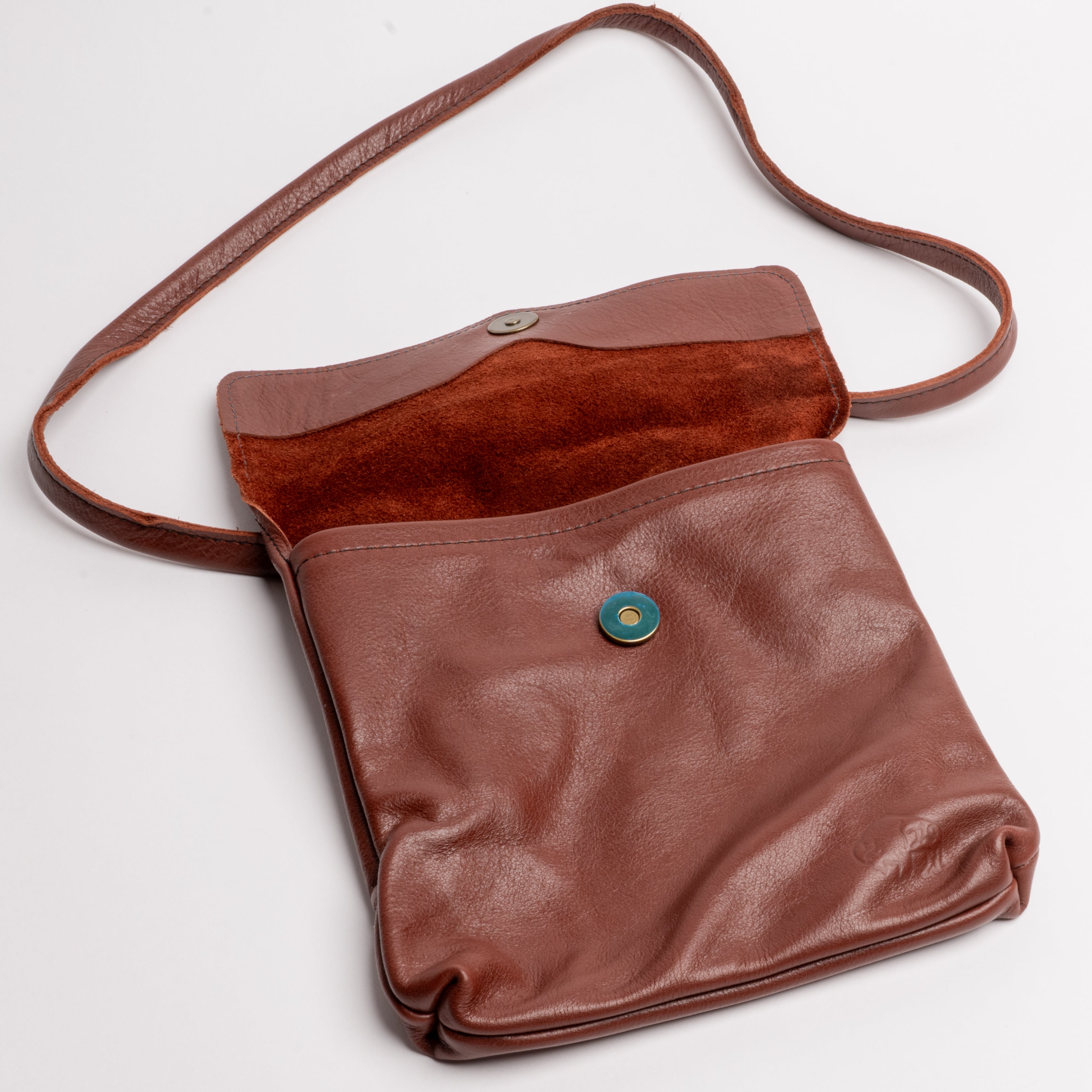 A brown leather shoulder bag with a matching strap, featuring a suede-like flap and a snap-button closure, photographed on a light gray background.