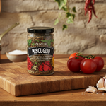 Jar of Olivelle Miscuglio on a wooden cutting board with tomatoes and garlic.