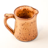 Ceramic pitcher with speckled brown glaze on a white background