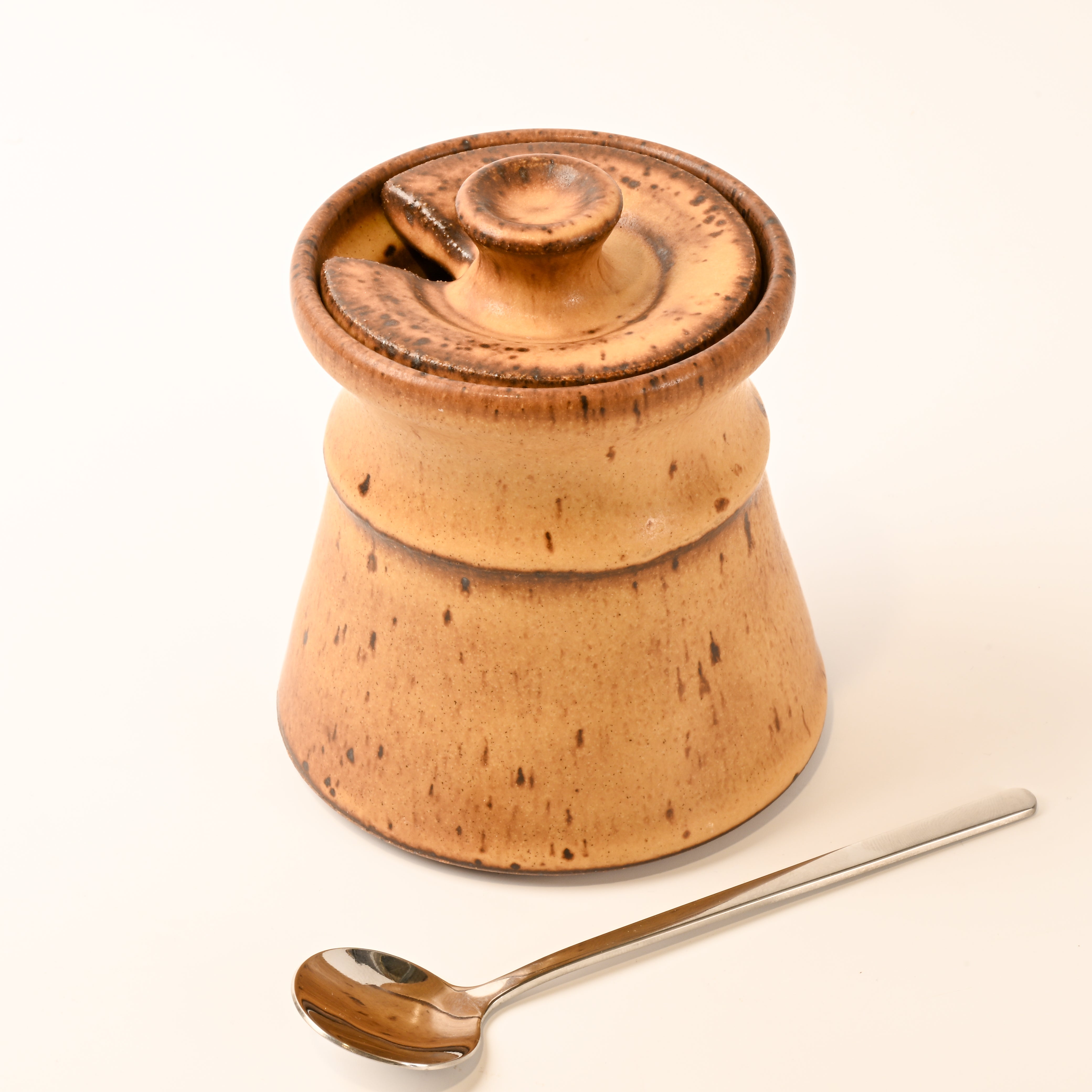 stoneware container with a lid and a spoon on a white background