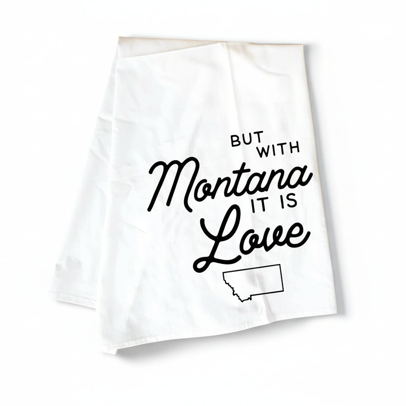 White towel with black text 'But with Montana it is Love' on a wooden surface