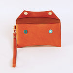 Brick colored leather clutch with a strap on a light beige background