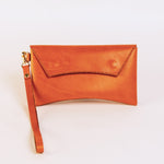 Brick colored leather clutch with a strap on a light beige background