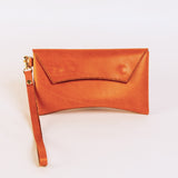 Brick colored leather clutch with a strap on a light beige background