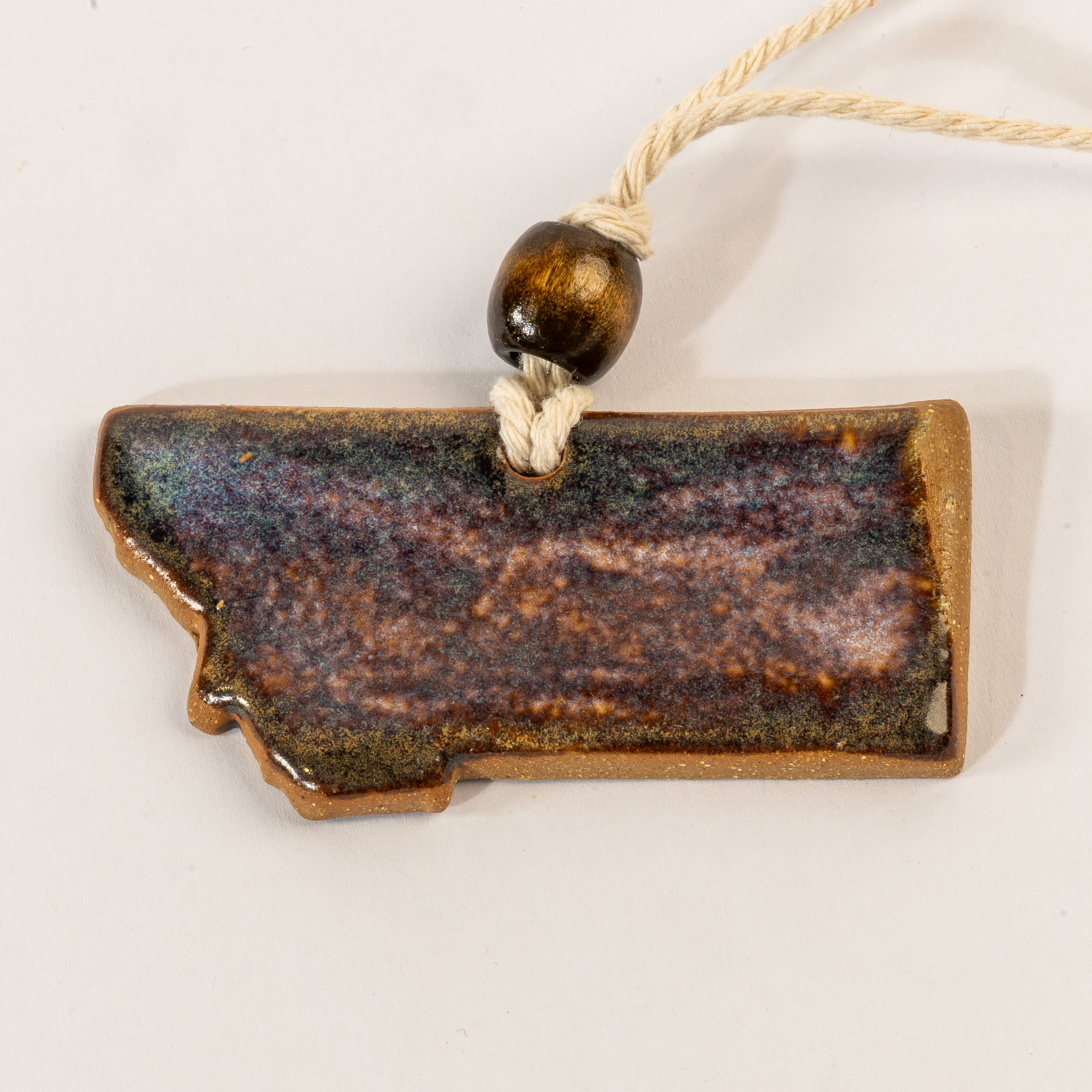 Ceramic pendant shaped like the state of Montana with a bead on a white background