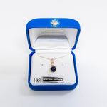 A rose gold pendant necklace with a round dark blue Montana sapphire stone, presented in an open blue Montana Jewelry box on a white background.