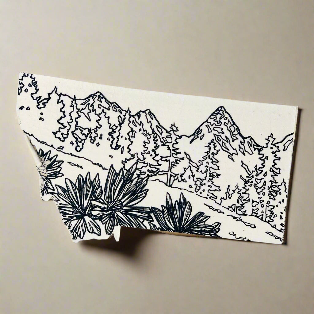 White dish cloth with black mountain and plant design on a light wooden surface.