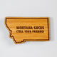 Wooden state-shaped sign with 'Montana Sucks (Tell Your Friends)' text on a white background
