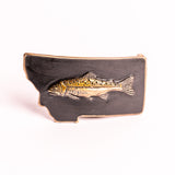 Metallic fish emblem on a black Montana-shaped belt buckle on a white background