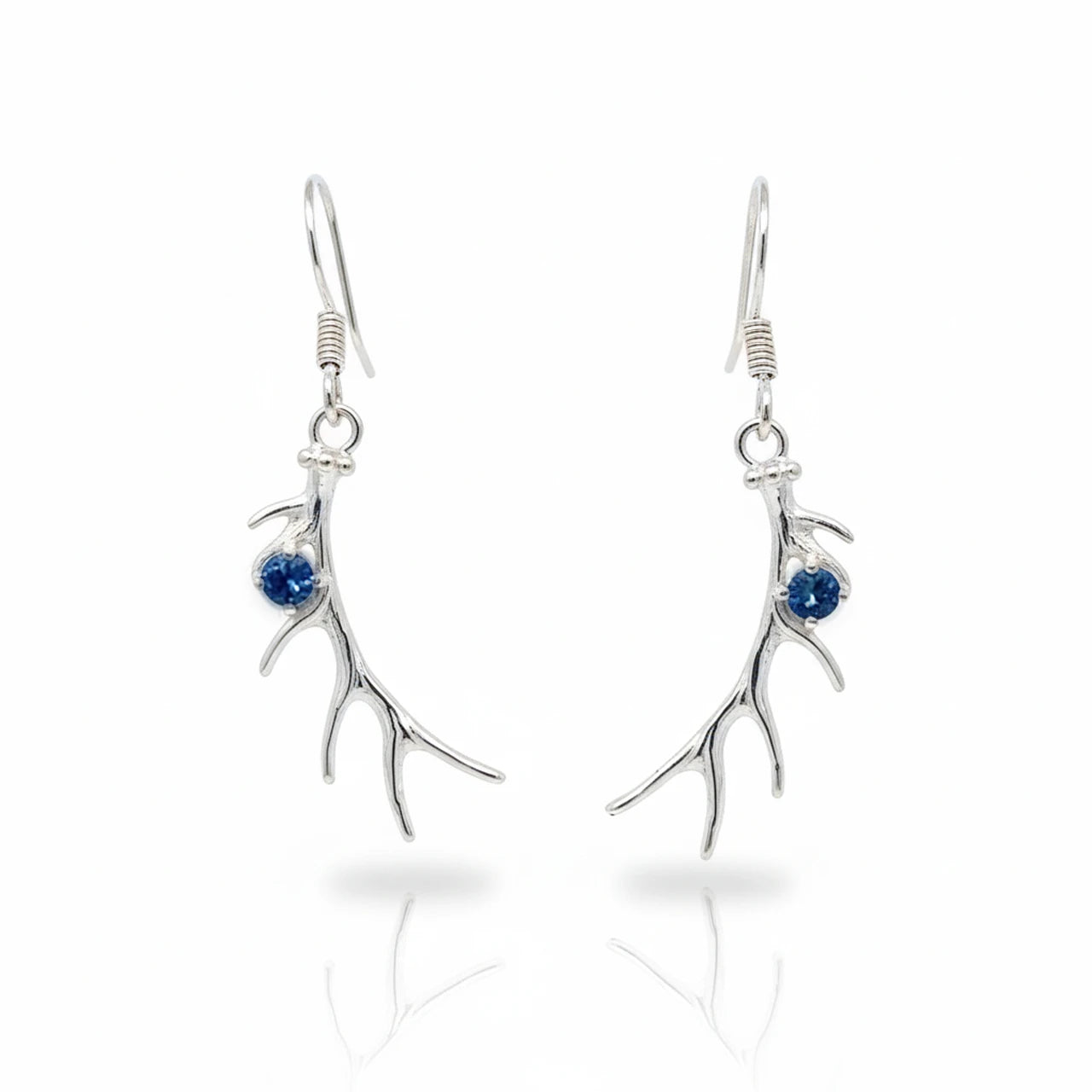 A pair of silver drop earrings shaped like antlers, each accented with a small round blue gemstone, shown on a clean white background with a soft reflection below.