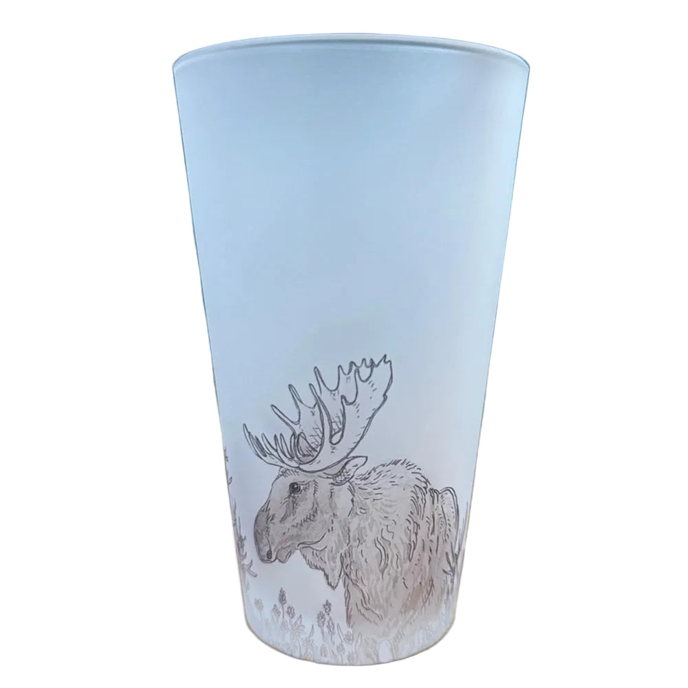 A frosted glass tumbler featuring a detailed line art illustration of a moose, displayed on a wooden surface with a dark teal tiled background. 