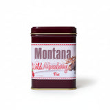 Mug with artistic design and Montana Wild Raspberry Tea canister on a tiled bathroom counter.
