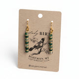 A pair of dangling earrings with green and gold spacer beads and gold hooks, displayed on a brown kraft paper card with 'Lady Bird' branding.