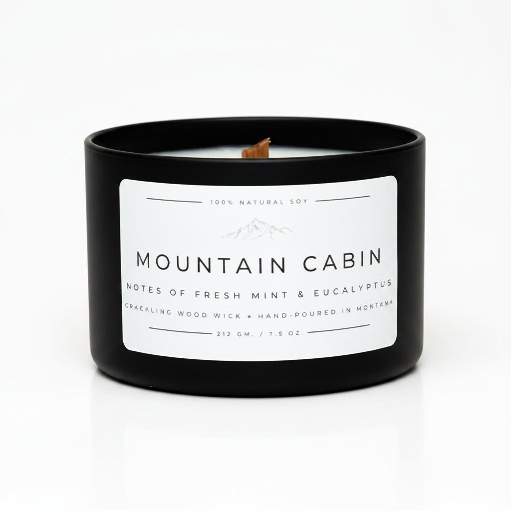 A black candle jar with a white label reading 'MOUNTAIN CABIN' and 'NOTES OF FRESH MINT & EUCALYPTUS,' sitting on a white background