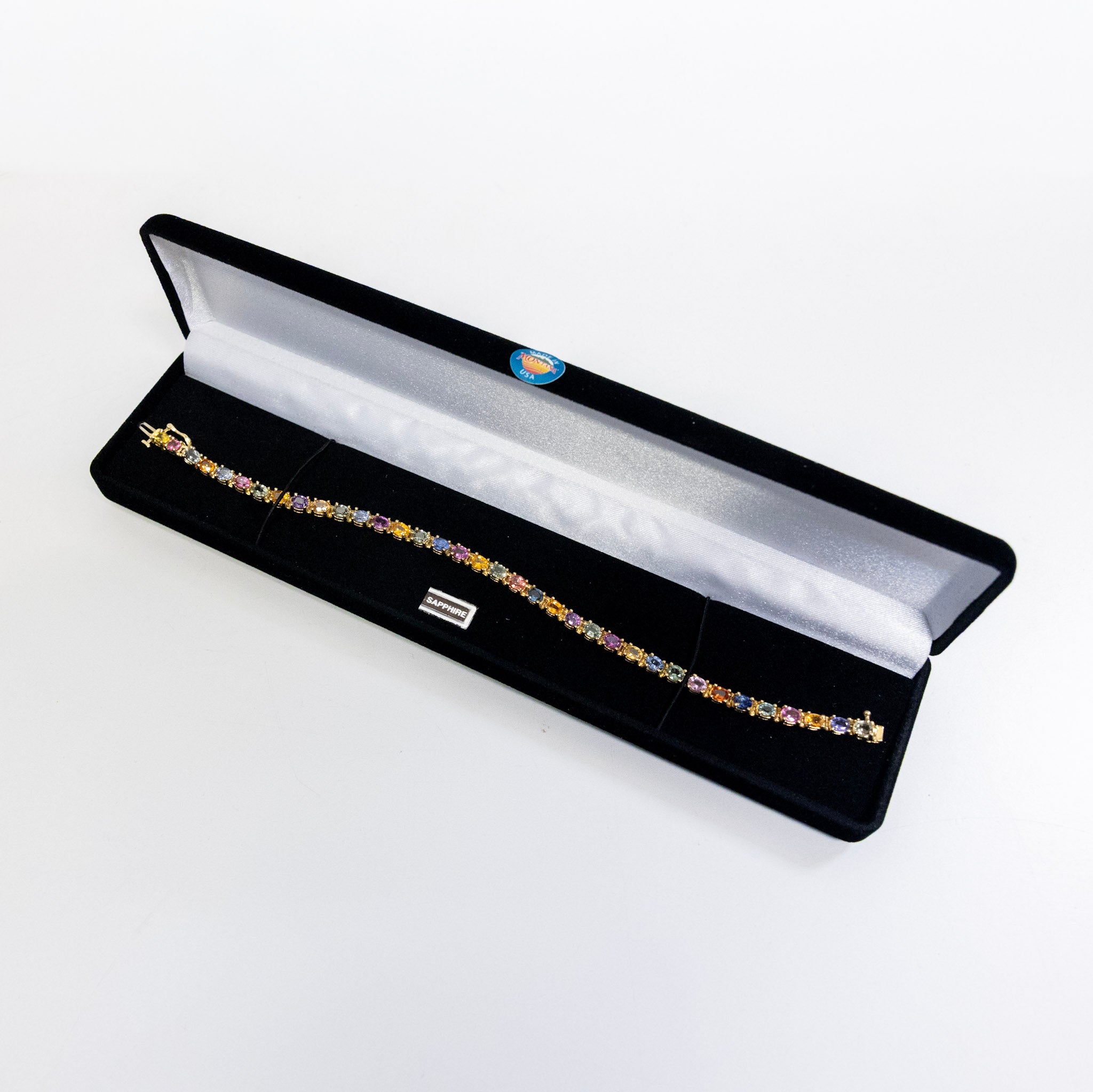 Bracelet with multicolored sapphire stones in a black jewelry box on a white background